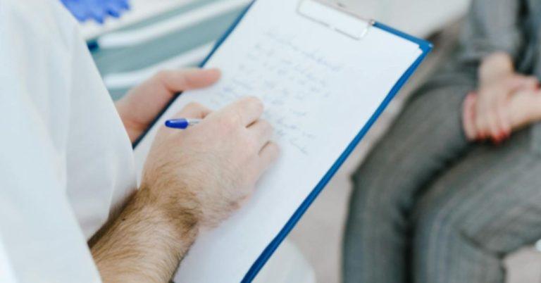 Læge skriver noter under samtale med patient om behandling ved Crohns sygdom.